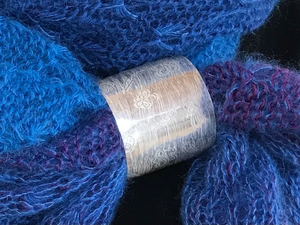 Taimi Design Breiter, gravierter Silberring mit feinem Muster umschließt einen blau-violetten Strickschal.