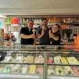 Eiscafé Venezia_Familie Schwarz Drei Personen präsentieren stolz bunte Eiscremekugeln hinter einer Vitrine mit vielfältigen Eissorten.