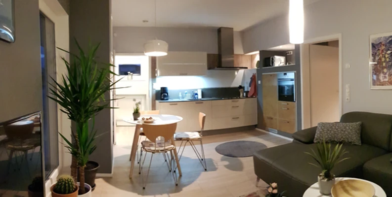 Moderne Wohnküche mit Holzfußboden, Esstisch, Ecksofa, Küchenzeile und stilvoller Beleuchtung.