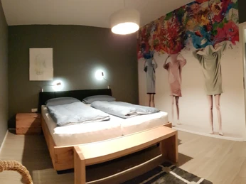 Weserpause1.jpg Modern gestaltetes Schlafzimmer mit grauen Wänden, Doppelbett, kunstvollem Wandmotiv und dezenter Beleuchtung.