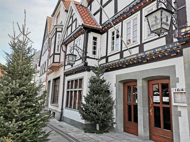 1643_Außenansicht_01 Fachwerkhäuserzeile mit winterlicher Dekoration und Tannenbäumen in historischer Altstadtstraße.