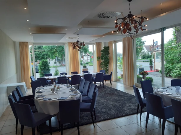 Eleganter Restaurantbereich mit gedeckten Rundtischen, blauen Stühlen und großen Fenstern.