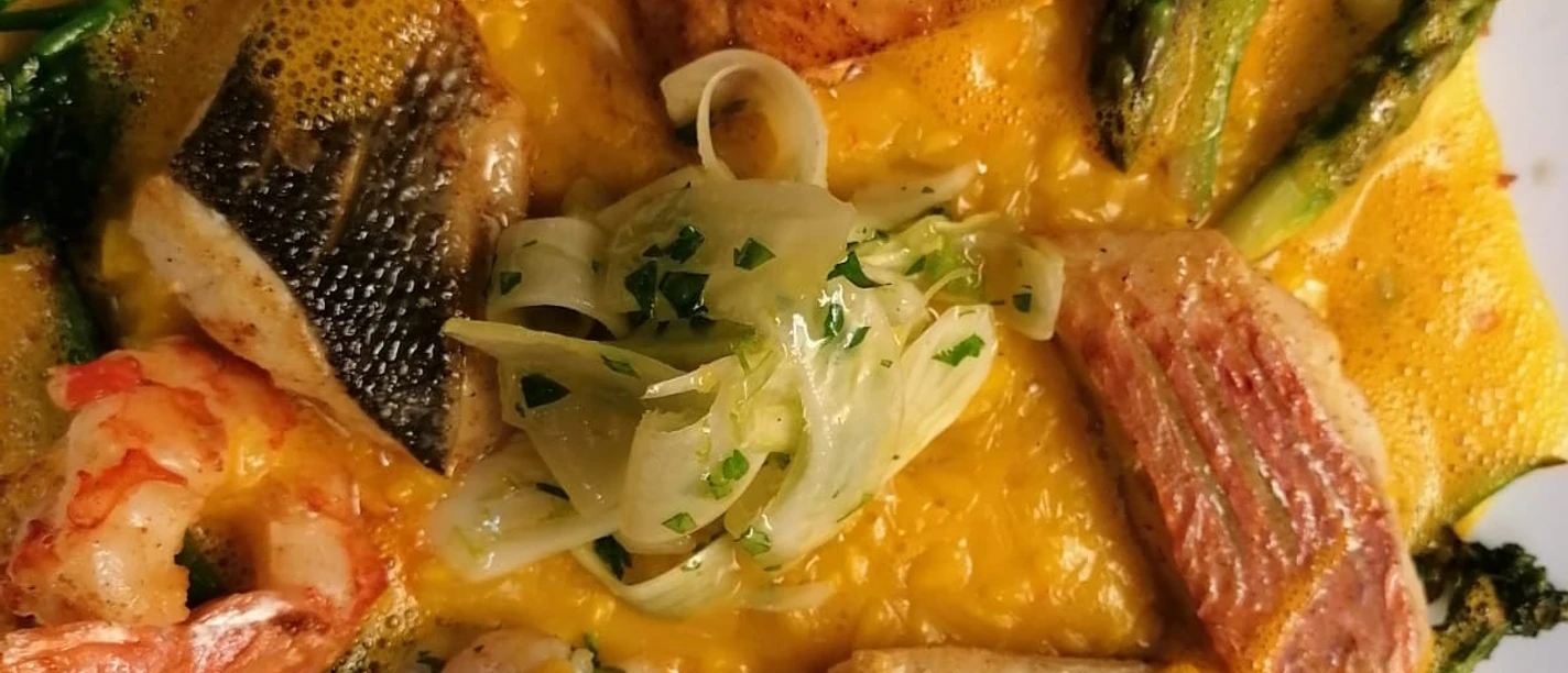 Domschenke_Speisen Verschiedene Fischstücke und Garnelen auf grünem Spargel, serviert mit Orangensoße und Fenchel.