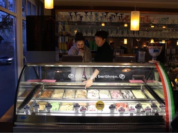 Gelateria Capri_Eisvariation In einer Eisdiele blickt ein Paar lächelnd auf eine beleuchtete Theke mit verschiedenen Eissorten.