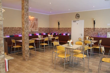 Gelateria Capri_Gastraum Gemütlicher Gastraum mit gelben Stühlen, Marmortischen, dekorativer Steinwand und bunter Beleuchtung.