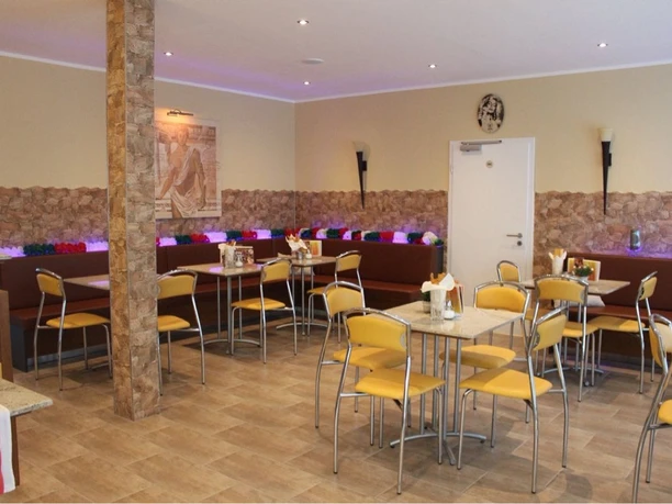 Gelateria Capri_Gastraum Gemütlicher Gastraum mit gelben Stühlen, Marmortischen, dekorativer Steinwand und bunter Beleuchtung.