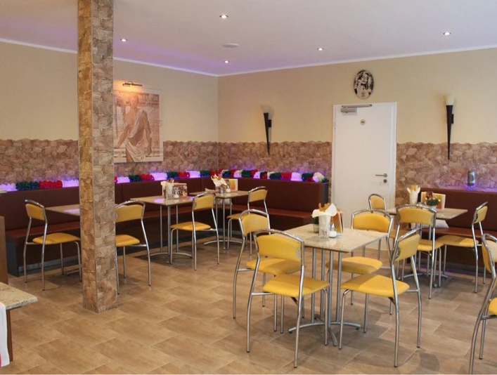 Gelateria Capri_Gastraum Gemütlicher Gastraum mit gelben Stühlen, Marmortischen, dekorativer Steinwand und bunter Beleuchtung.