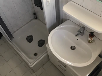 Gartenblick (4).jpeg Barrierefreies Badezimmer mit ebenerdiger Dusche, Waschbecken, Toilette und hellen Fliesen.