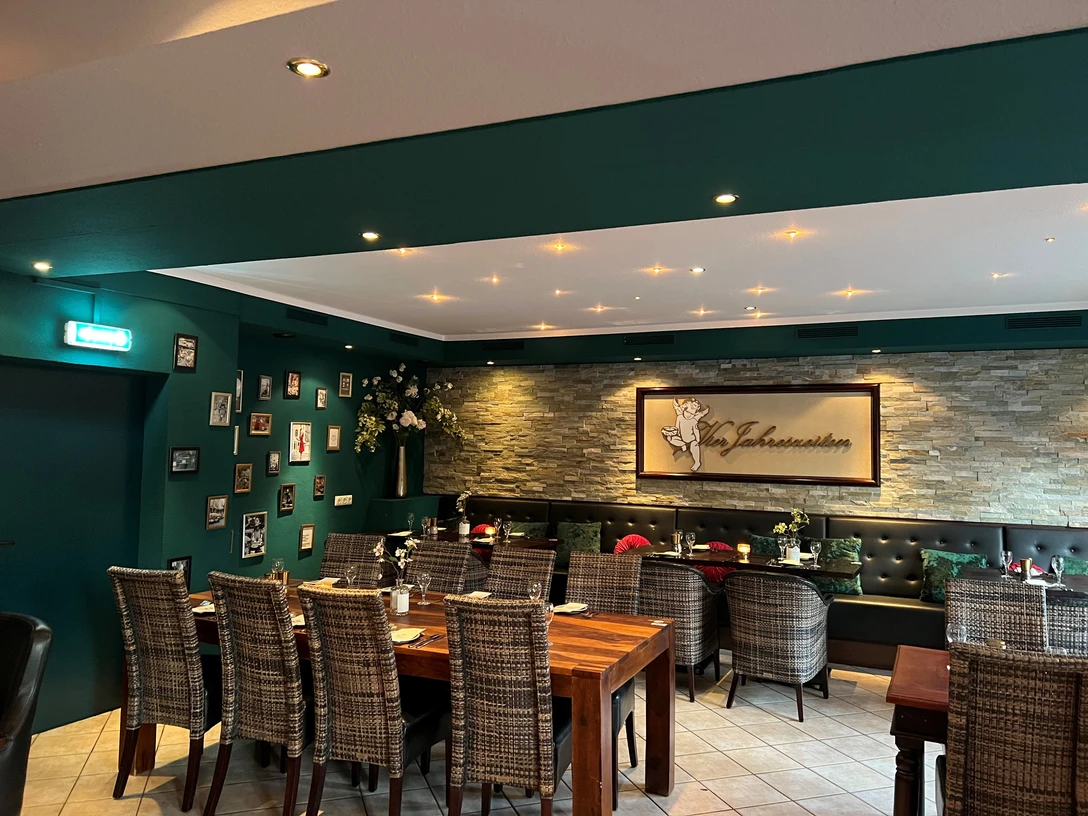 Vier Jahreszeiten Marklohe Gemütliches Restaurant mit Rattanstühlen, dekorativer Steinwand und gedeckten Tischen für Gäste.