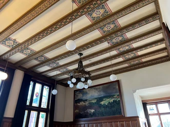 Ratssaal Rathaus Hoya Holzvertäfelter Ratssaal mit prunkvollem Kronleuchter, gemusterten Deckenbalken und bemaltem Wandbild.