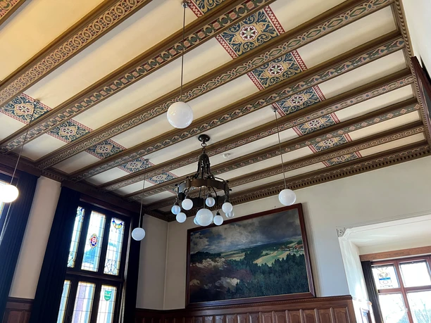 Ratssaal Rathaus Hoya Holzvertäfelter Ratssaal mit prunkvollem Kronleuchter, gemusterten Deckenbalken und bemaltem Wandbild.