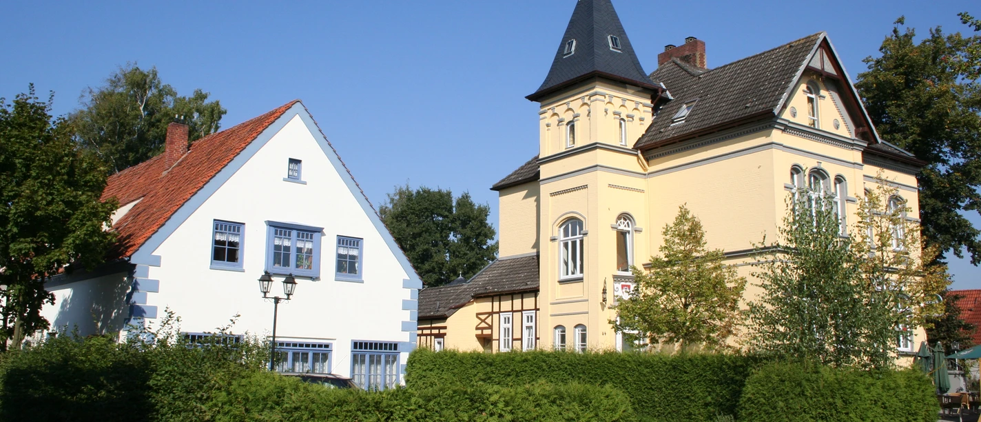 Historisches Rathausensemble mit gelbem Turmgebäude und benachbartem weißen Fachwerkhaus.