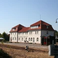 Bahnhof Hoya in Niedersachsen: Historisches Gebäude mit rotem Dach und weißen Fassaden, Gleise im Vordergrund.