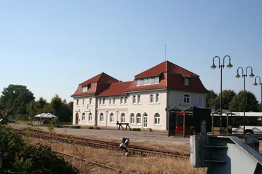 Bahnhof Hoya Bahnhof Hoya in Niedersachsen: Historisches Gebäude mit rotem Dach und weißen Fassaden, Gleise im Vordergrund.