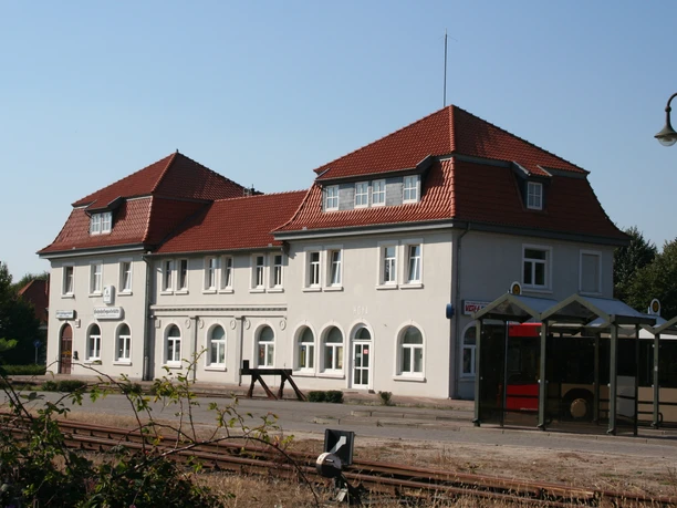 Bahnhof Hoya Bahnhof Hoya mit rotem Ziegeldach, weißen Wänden und einem Bahnsteig im Vordergrund bei klarem Himmel.