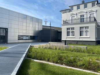 Deutsches Schloss- und Beschlägemuseum in Velbert Museum mit moderner Fassade und angrenzendem historischem Gebäude, umgeben von Grünflächen unter blauem Himmel.