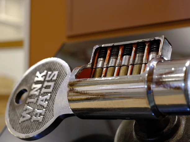 Exponat des Deutschen Schloss- und Beschlägemuseums in Velbert Nahaufnahme eines metallischen Schlosszylinders mit Schlüssel, sichtbar sind die Stiftzuhaltungen.