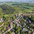 Stadt Oerlinghausen – Fotograf Patrick Piecha Luftaufnahme einer grünen Hügelstadt mit vielen Häusern, einer Kirche und umgeben von Wäldern.