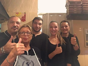 Fünf Personen in einem Restaurant, lächelnd und mit erhobenen Daumen, die Herzlichkeit ausstrahlen.