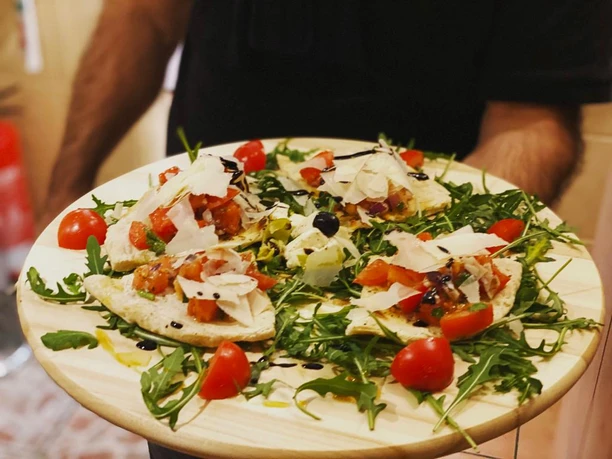 Ein Teller mit belegten Fladenbroten auf Rucola, garniert mit Tomaten, Balsamico und Parmesan.