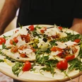 Pizzeria Due_Speisen Ein Teller mit belegten Fladenbroten auf Rucola, garniert mit Tomaten, Balsamico und Parmesan.