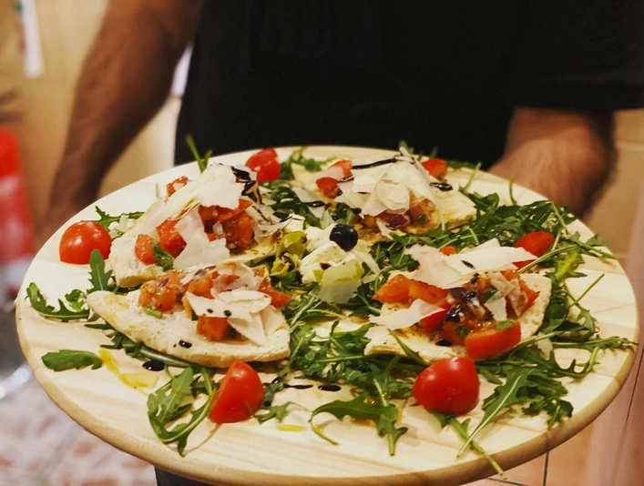 Pizzeria Due_Speisen Ein Teller mit belegten Fladenbroten auf Rucola, garniert mit Tomaten, Balsamico und Parmesan.