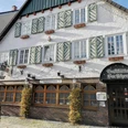 Gaststätte Bartscher_Außenansicht Traditionelles Fachwerkgebäude mit grünen Fensterläden, darunter das Schild "Gaststätte Bäcker".
