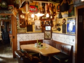 Gemütlicher Gastraum eines rustikalen Wirtshauses mit Holztisch, Wanddeko und alten Werbeschildern.