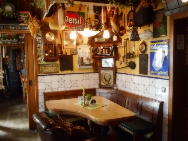 Gemütlicher Gastraum eines rustikalen Wirtshauses mit Holztisch, Wanddeko und alten Werbeschildern.