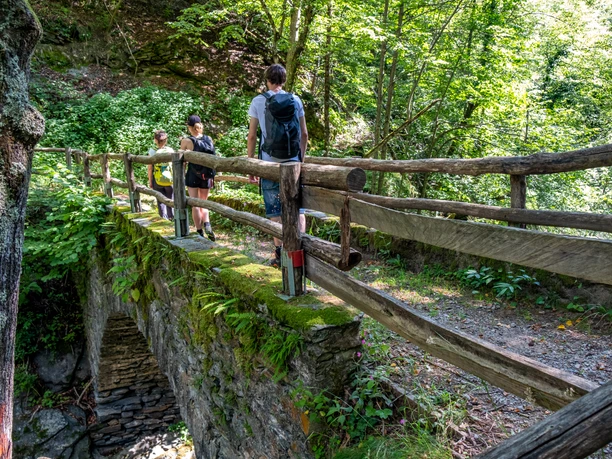 ViaStockalper - Wanderer auf einer Steinbrücke im Wald ViaStockalper - Wanderer auf einer Steinbrücke im Wald