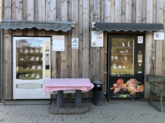 Fleischautomat am Grimberghof Zwei Automaten an einer Holzwand bieten verschiedene Waren, einer mit Fleischprodukten und außen ein Tisch.