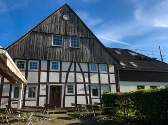 Ein traditionelles Fachwerkgebäude mit holzverkleidetem Giebel und aufgestellten Gartenmöbeln.