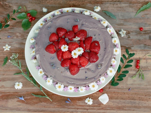 Naturfreundehaus Kuchen Erdbeertorte mit Schokoladenmousse, dekoriert mit Gänseblümchen, auf rustikalem Holztisch.