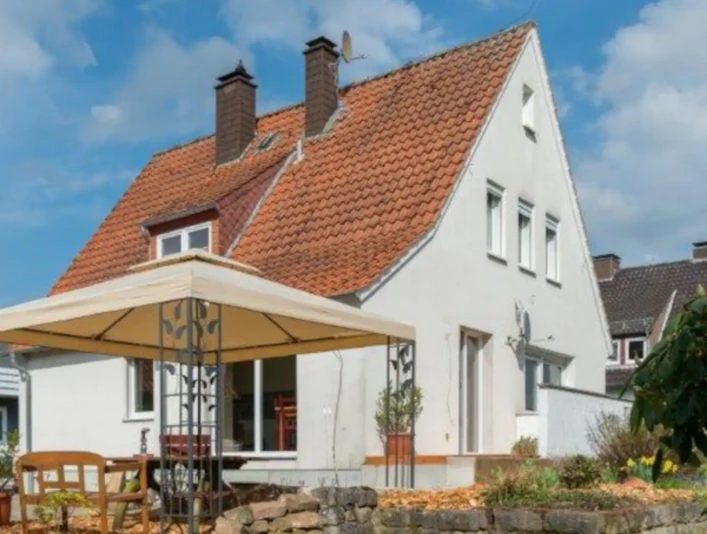 Ferienhaus Westerkamp Freistehendes weißes Ferienhaus mit rotem Ziegeldach, Gartenpavillon und blühenden Beeten.