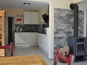 Moderne Wohn- und Essküche mit weißer Küchenzeile, Holztisch, Kamin und Wandschränken.