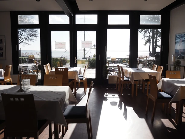 San Stefan Ein lichtdurchfluteter Raum mit gedeckten Tischen und Blick durch große Fenster auf die sonnige Küste.