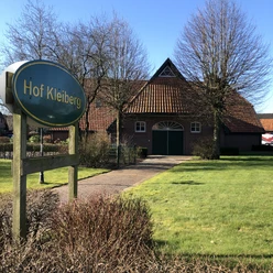 Hof Kleiberg Das Bild zeigt den Hof Kleiberg mit einem traditionellen Backsteingebäude und grünem Rasen im Vordergrund.