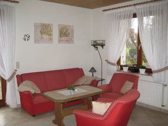 Wohnzimmer mit roten Sofas, Holztisch, weißer Wanddekoration und großen Fenstern mit Vorhängen.