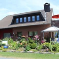 Haus Heidegarten.jpg Zweistöckiges Backsteinhaus mit gepflegtem, blühendem Garten und einem markanten Pavillon davor.