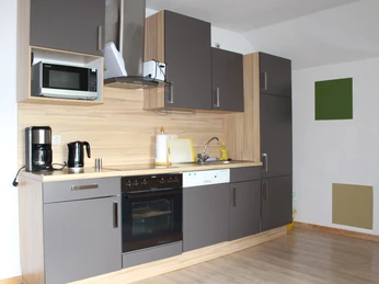 Moderne Einbauküche mit Geräten, Holzoptik, graue Schränke, Mikrowelle, Kaffeemaschine und Spüle.