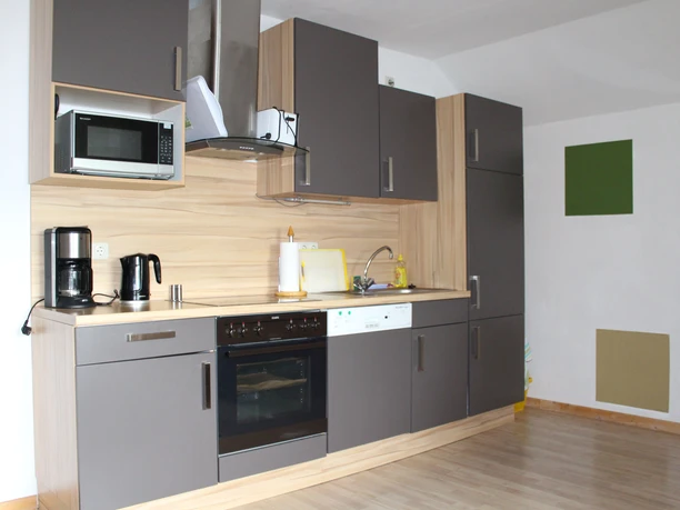 Küche FW Balkon.jpg Moderne Einbauküche mit Geräten, Holzoptik, graue Schränke, Mikrowelle, Kaffeemaschine und Spüle.