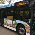 HeideShuttle Bus mit Landschaftsmotiven, Schafen und Heide beklebt. Tür offen, Fahrgäste steigen ein.
