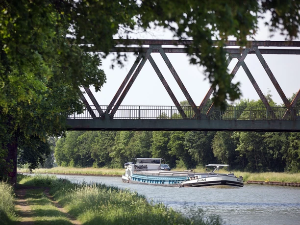 Lübbecke Mittellandkanal Oliver Krato Ein langes Frachtschiff fährt unter einer Eisenbahnbrücke auf dem Mittellandkanal entlang.