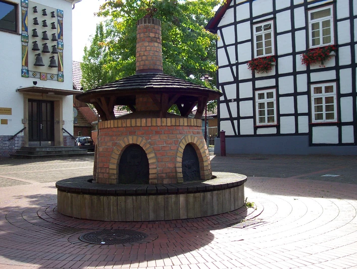 Glindower Platz Rahden Runder Backofen mit roten Ziegeln auf einem gepflasterten Platz, umgeben von Fachwerkhäusern.