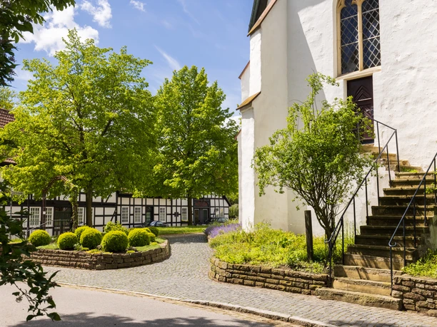 Stemwede-Levern Fachwerkhäuser und eine alte Kirche mit großem Treppenaufgang, umgeben von grünen Bäumen und Sträuchern.