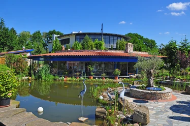 Rila erleben Taverne Taverne mit rotem Ziegeldach und Glasfront, umgeben von Teich und grüner Gartenlandschaft.