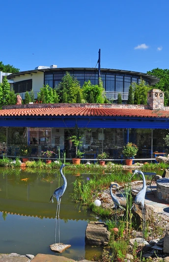 Rila erleben Taverne Taverne mit rotem Ziegeldach und Glasfront, umgeben von Teich und grüner Gartenlandschaft.