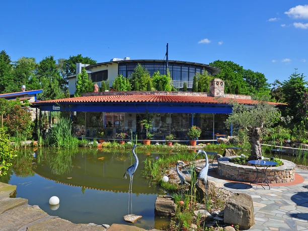 Rila erleben Taverne Taverne mit rotem Ziegeldach und Glasfront, umgeben von Teich und grüner Gartenlandschaft.