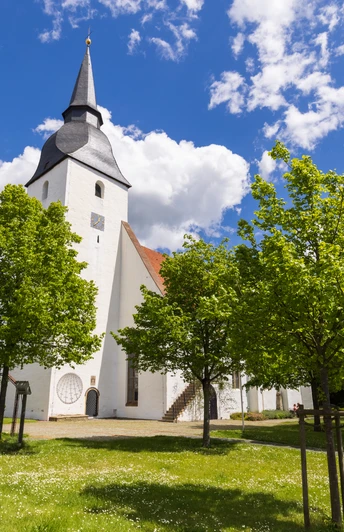 Stiftskirche Levern Weiße Stiftskirche Levern mit markantem Turm, umgeben von grünen Bäumen und blauem Himmel.