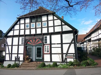 Fachwerkhaus mit markanter Architektur, bunte Tür, gepflegte Vorgartenanlage, blauer Himmel.